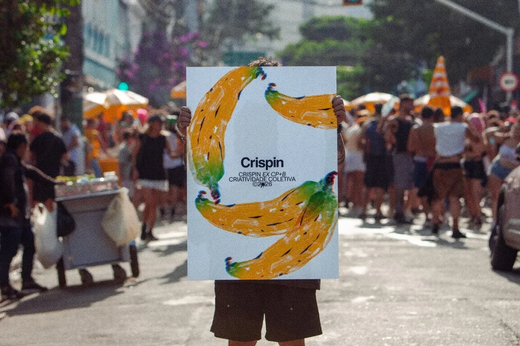 Profissionais de marketing em reunião comemorando o rebranding da agência CP+B para Crispin, exibindo o novo logo e slogan 'Criatividade Coletiva'